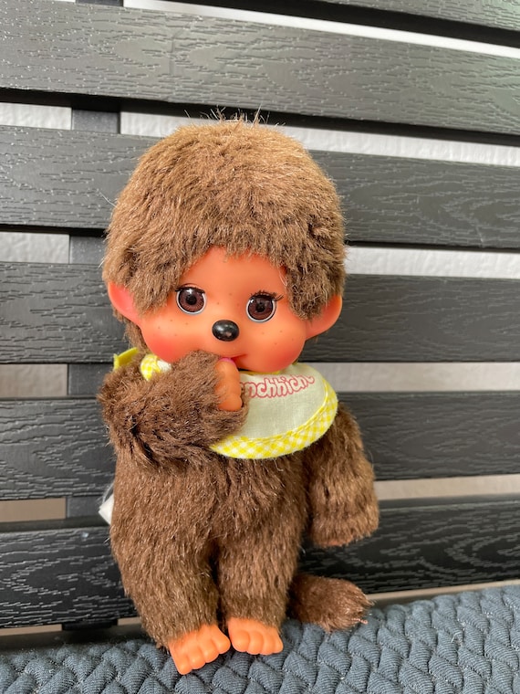 茶色のかわいいモンチッチのまばたき目が親指を吸っているぬいぐるみ